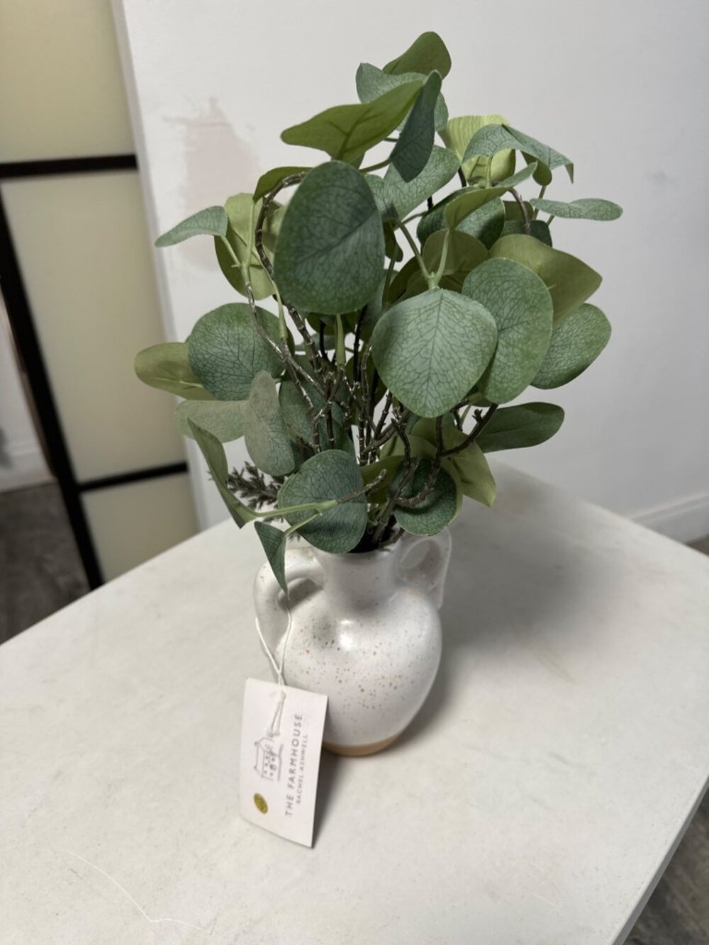 Arreglo decorativo artificial de eucalipto colocado en un pequeño jarrón de cerá